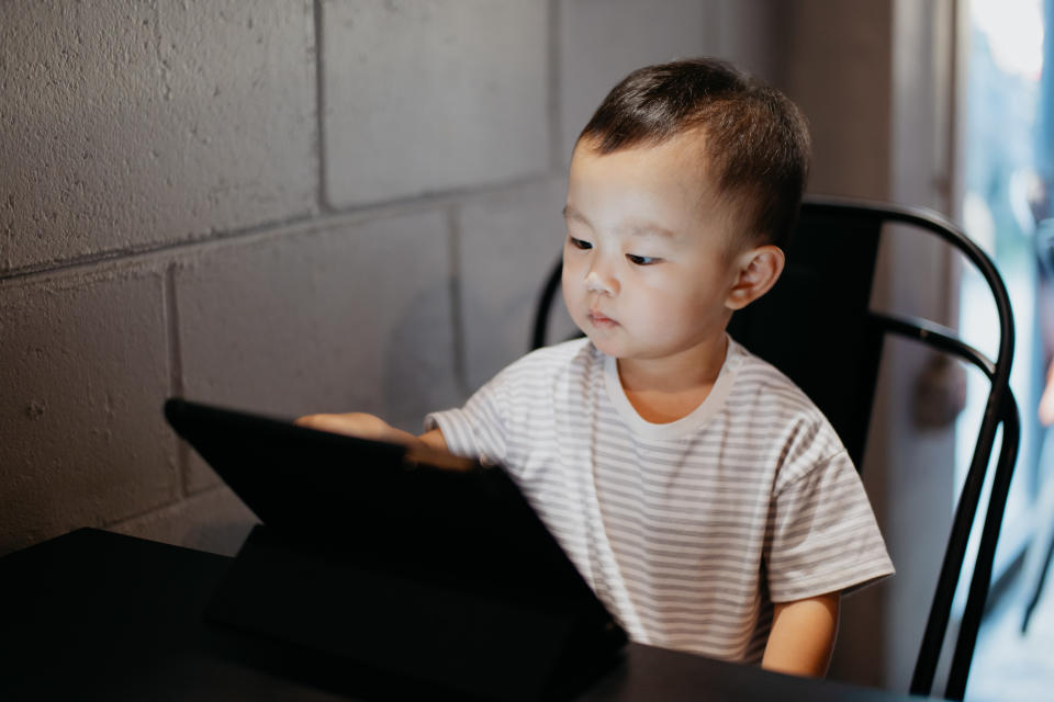 A young child sits at a table, focused on touching a tablet screen