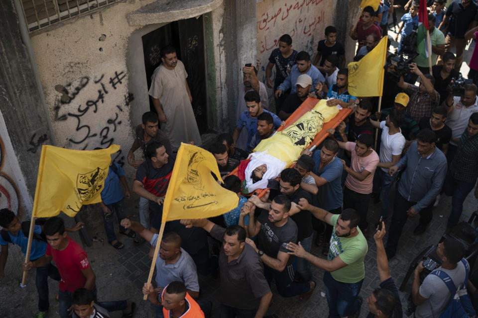 In this Sept. 15, 2018 photo, Palestinians carry the body of 11-year-old Shady Abdel-al during his funeral in Beit Lahiya, northern Gaza Strip. As the boy's body is carried through the neighborhood, it is surrounded by a sea of yellow flags of the Palestinian Fatah party and former guerrilla movement founded by Yasser Arafat. But when it reaches the mosque, there is another huge group of teenagers waiting with the green flag of Hamas. (AP Photo/Felipe Dana)