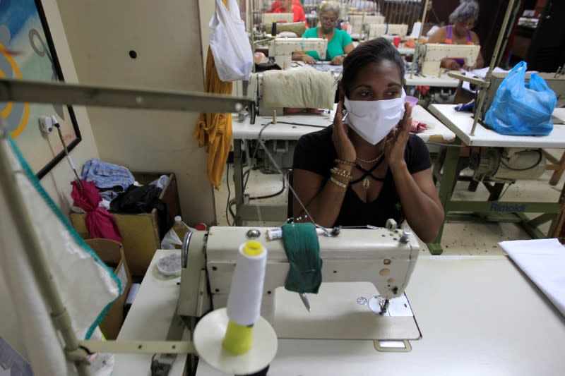 A seamstress poses with a cloth face mask to be sold in an adjoining clothing store, in Havana