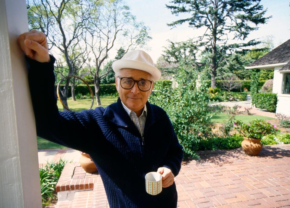 Norman Lear holding a coffee mug and leaning on the side of a door