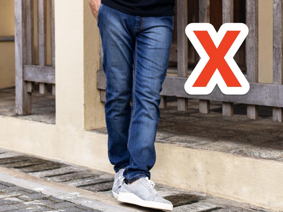 red x next to person wearing dark-wash jeans on a street