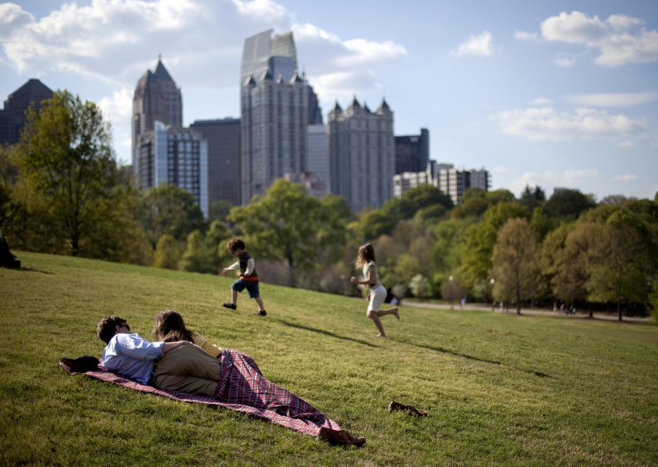 FILE - In this March 25, 2012, file photo, a couple enjoy a sunny afternoon against the backdrop of the Midtown skyline from Piedmont Park in Atlanta. Like New York’s Central Park, the nearly 200-acre green space in Midtown gives Atlanta residents and visitors a tranquil setting to picnic, play games, walk their dogs and relax in the meadow or along the shores of Lake Clara Meer. The park also plays host to major city events. The annual 10-kilometer Fourth of July Peachtree Road Race ends there and the Dogwood Festival and Music Midtown festival are held there. (AP Photo/David Goldman, File)