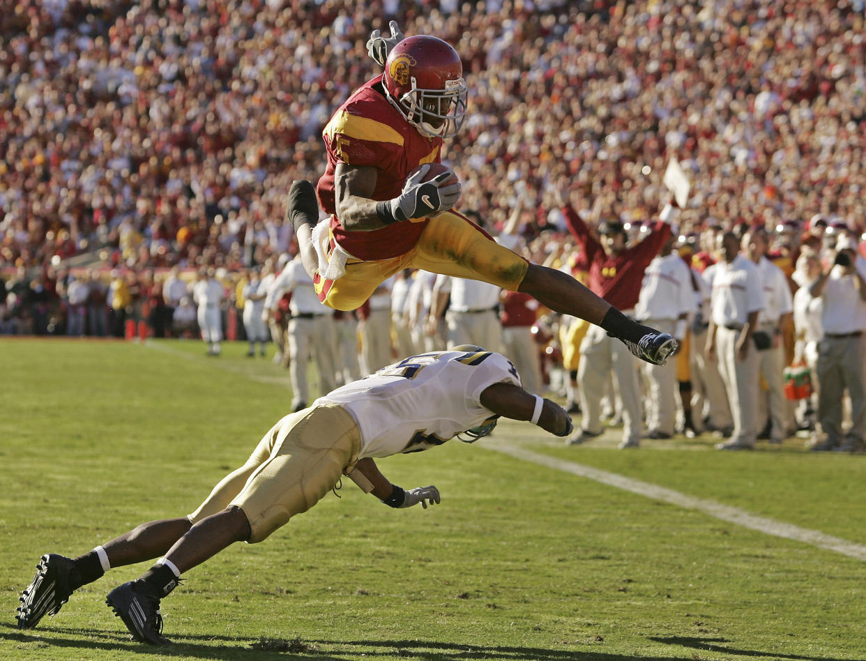 FILE - Southern California's Reggie Bush leaps over UCLA defender Marcus Cassel as he rushes 13 yards for a touchdown in the second quarter of an NCAA college football game at the Los Angeles Memorial Coliseum, Saturday, Dec. 3, 2005. Reggie Bush, whose Heisman Trophy victory for Southern California in 2005 was vacated because of NCAA violations, was among 18 players in the latest College Football Hall of Fame class announced Monday, Jan. 9, 2023. (AP Photo/Chris Carlson, File)