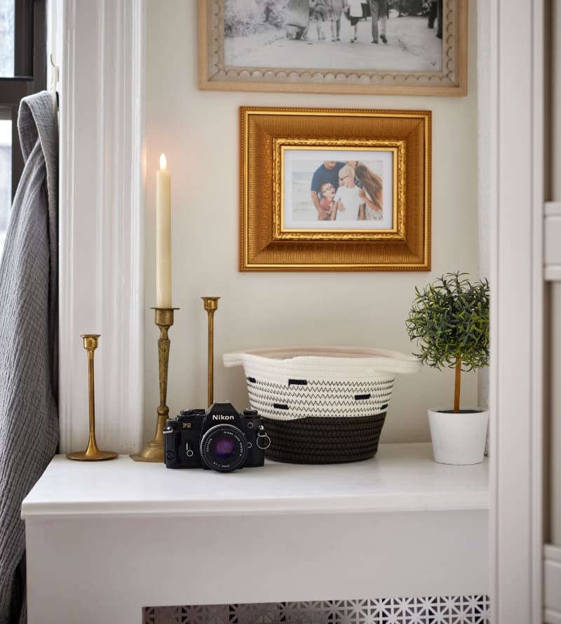 Photos hang above candles, camera, basket, and plant on top of covered radiator.