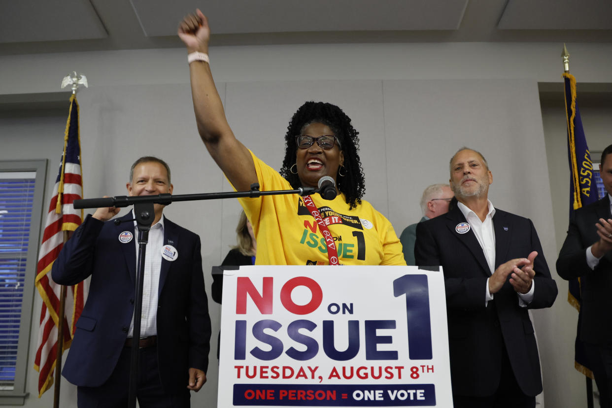 Deidra Reese stands behind a podium with a sign that reads: No on Issue 1.