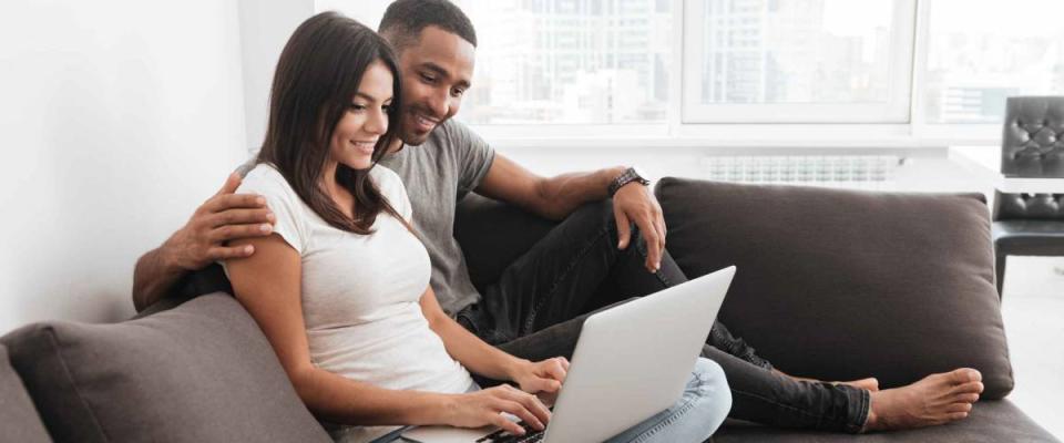 Cheerful young couple smile together while using laptop indoor. Look at laptop.