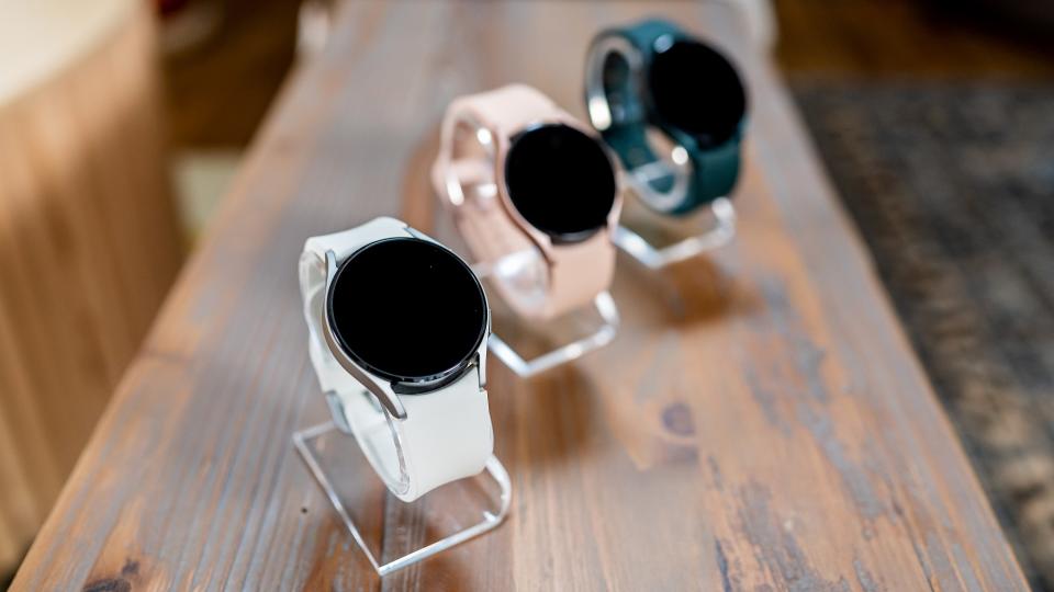 Lineup of three Samsung Galaxy Watch 4 smartwatches on wooden table at Galaxy Unpacked launch event.