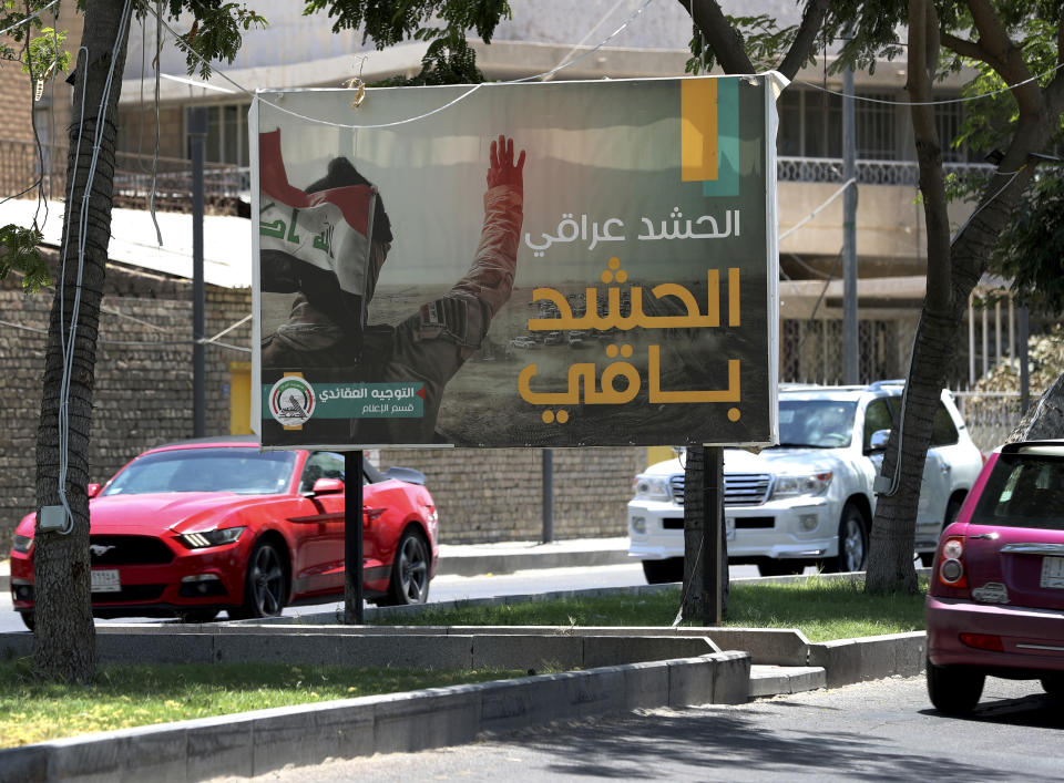 In this Tuesday, July 2, 2019 photo, motorists pass by a Popular Mobilization poster in Baghdad, Iraq. The Iraqi government's move to place Iranian-backed militias under the command of the armed forces is a political gamble by a prime minister increasingly caught in the middle of a dangerous rivalry between Iran and the U.S., the two main power brokers in Iraq. (AP Photo/Hadi Mizban)