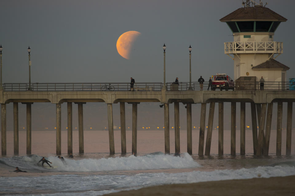 HUNTINGTON BEACH, CA. - JANUARY 31: A surfer rides a wave as the super blue blood moon eclipse sets over the  Huntington Beach pier January 31, 2018. (Photo by Allen J. Schaben/Los Angeles Times via Getty Images)