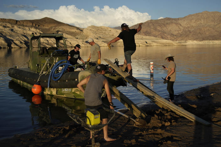 Dave Kiley, also know as Diesel Dave, boards a boat while helping to free a beached houseboat with the crew from the youtube channel HeavyDSparks at the Lake Mead National Recreation Area, Thursday, June 23, 2022, near Boulder City, Nev. The crew of the youtube channel hauled a houseboat stranded by falling water levels back into the water. (AP Photo/John Locher)