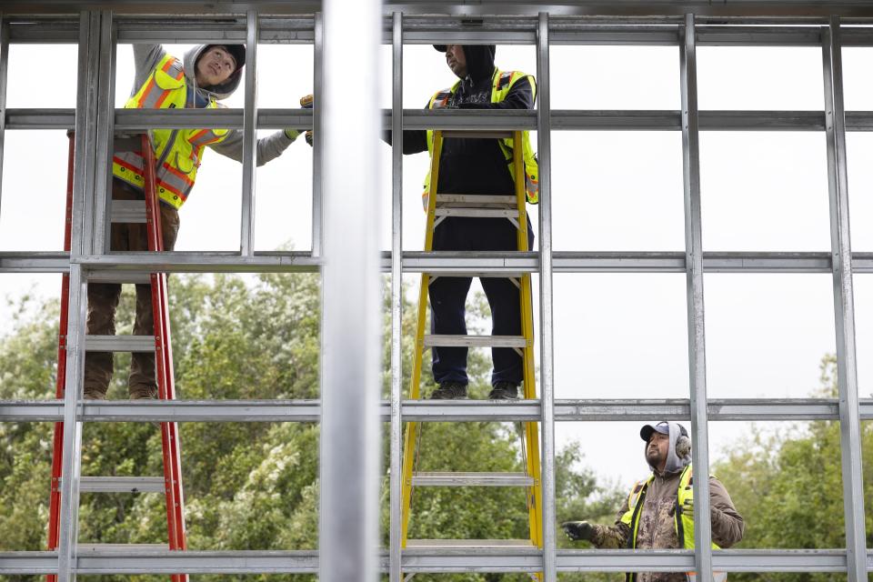 Alaska Native Tribal Health Consortium workers install side paneling for a lift house on Qugtuliaq Road, Thursday, Aug. 17, 2023, in Akiachak, Alaska. Installing the hookups required connecting and burying water and sewer mains, building two additional lift stations, and providing interior plumbing in every home — kitchen and bathroom sinks, a toilet, a shower and ventilation. (AP Photo/Tom Brenner)