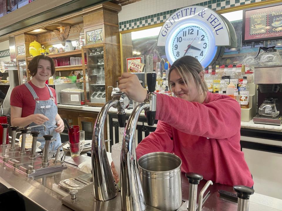 Malli Jarrett, right, serves up drinks from the soda fountain while co-worker Nathaniel Fornash watches at Griffith & Feil Drug on Thursday, March 30, 2023, in Kenova, W. Va. Soda fountains were often in pharmacies because pharmacists mixed tonics meant to heal ailments. Now they're preserving a style of living and an attitude that was common in little towns across America. (AP Photo/John Raby)