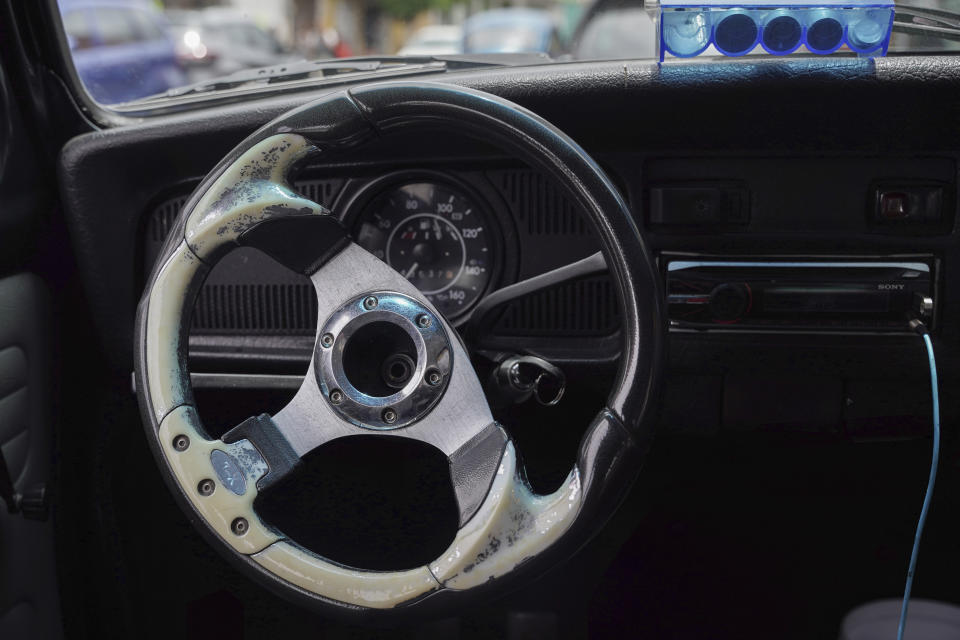 Un volante desgastado de estilo de competición y un dispensador de monedas se ven en el interior de un Beetle de Volkswagen de la taxista Janette Navarro, en el vecindario de Cuautepec, de Ciudad de México, el viernes 21 de junio de 2024. Navarro comenzó a manejar vochos para trabajar hace ocho años como una forma de mantener a sus tres hijos y pagarles los estudios. (AP Foto/Aurea Del Rosario)