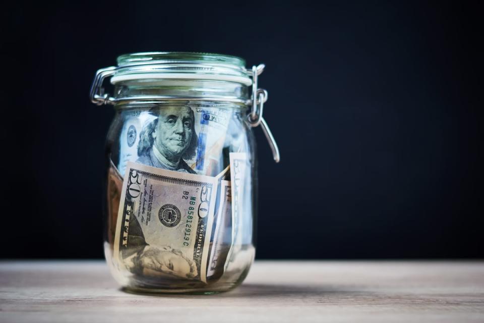 A glass jar full of dollar bills on a wooden table.