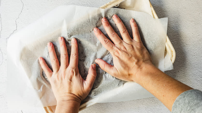hands pressing parchment paper down on pan