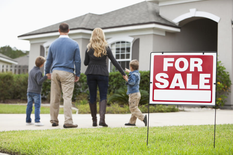 Family with two boys (4 and 6 years) standing in front of house with FOR SALE sign in front yard.  Source: Getty Images