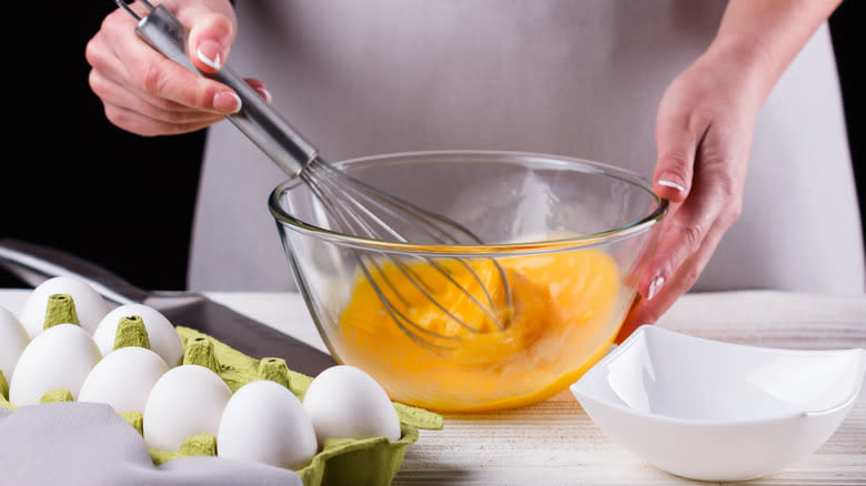 Person whisking eggs in a glass bowl