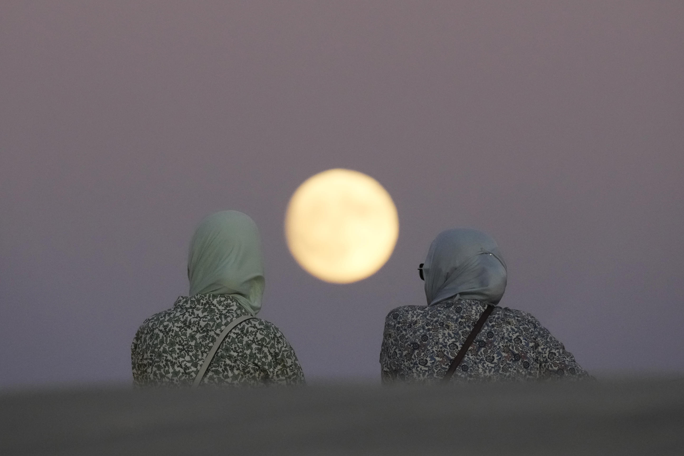 Two women watch a nearly full supermoon rise in Lisbon, Portugal, on Monday.