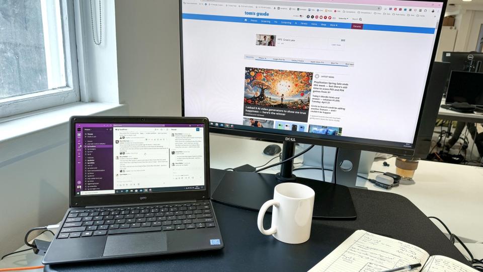 The Geobook 2E budget laptop on a desk in front of an external monitor in a brightly lit office