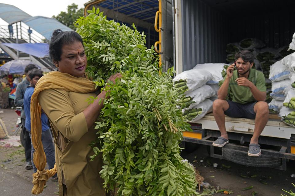 Preethi, a 38-year-old transgender woman who uses only her first name, carries a bunch of vegetables for her customer who hired her electric auto rickshaw for a ride in Bengaluru, India, Monday, July 10, 2023. “I have regular customers who range from vegetable vendors to mothers in my neighborhood who prefer to send their daughters to schools and colleges with me,” said Preethi. (AP Photo/Aijaz Rahi)