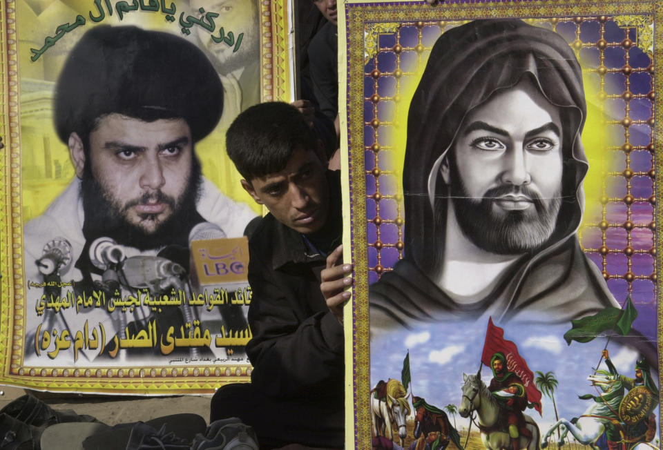 FILE - An Iraqi sits between posters of prominent Shiite cleric Sheik Muqtada al-Sadr, left, and Imam Ali, the first Imam and cousin of prophet Muhammed during Friday prayers in the largest Shiite Muslim enclave in Baghdad, Friday Nov. 14, 2003. Al-Sadr is a populist cleric, who emerged as a symbol of resistance against the U.S. occupation of Iraq after the 2003 invasion. ( AP Photo/Samir Mizban, File)