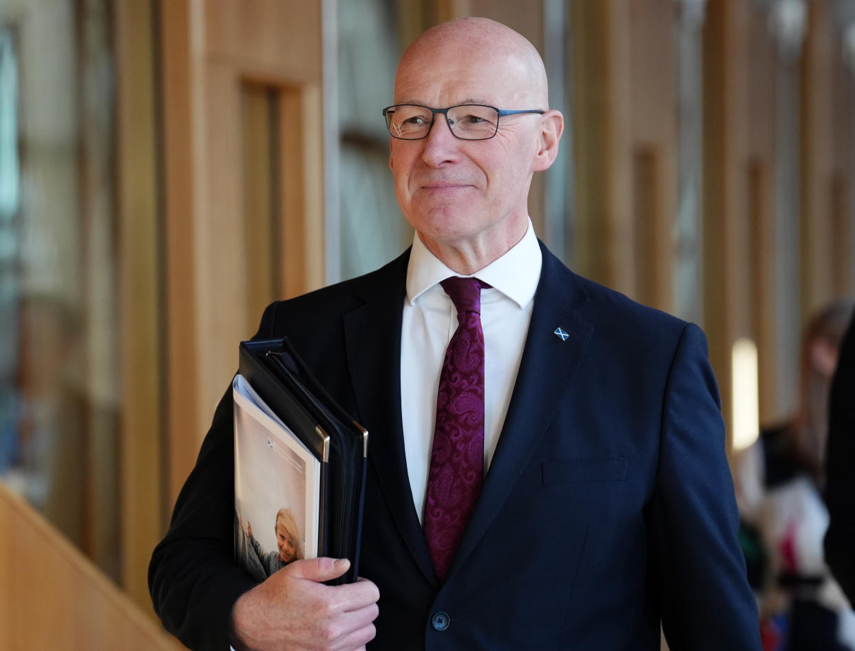 First Minister John Swinney smiles as he walks into the Scottish Parliament chamber