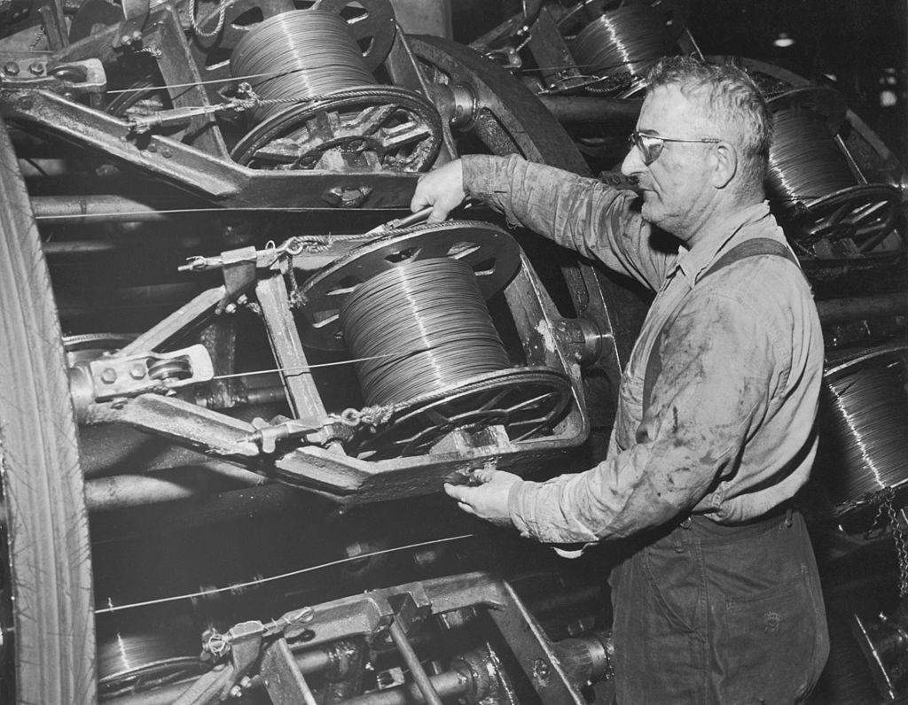 A man adjusts a spool of wire on a wire rope machine, USA, circa 1940.