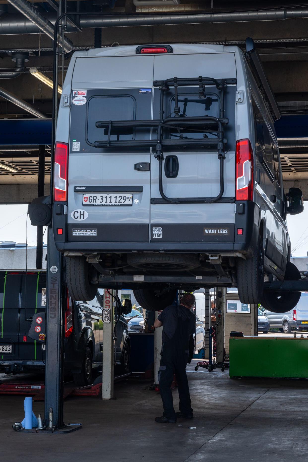 Odense, Denmark - 10 June, 2021: gray camper van in a modern garage up on the car lift  with a car mechanic underneath