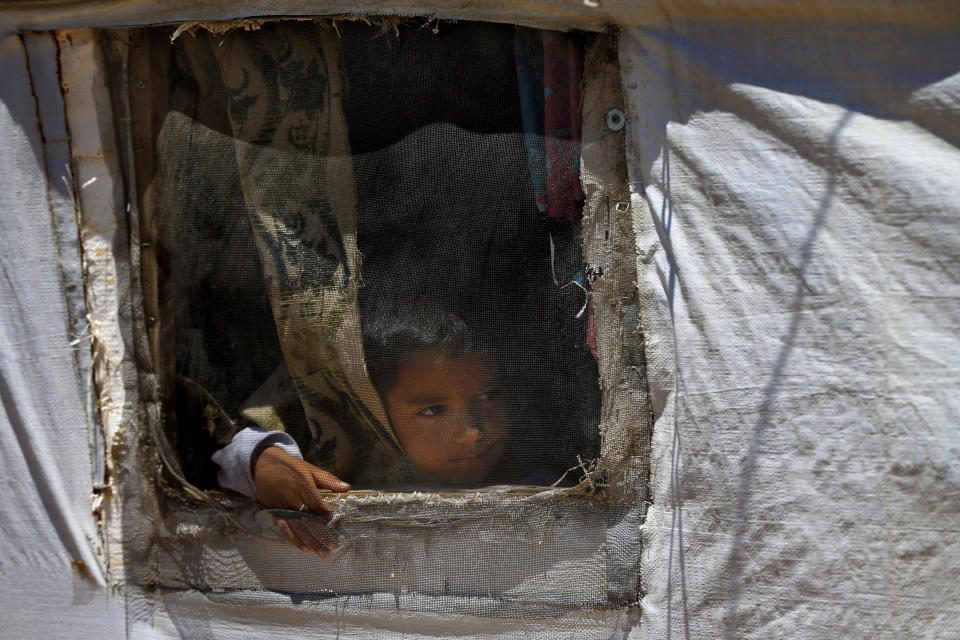 In this Sunday, June 16, 2019 photo, a Syrian refugee child looks through a window in his family tent in a refugee camp in the eastern Lebanese border town of Arsal, Lebanon. Authorities in Lebanon are waging their most aggressive campaign yet against Syrian refugees, making heated calls for them to go back to their country and taking action to ensure they can’t put down roots. They are shutting down shops where Syrians work without permits and ordering the demolition of anything in their squalid camps that could be a permanent home. (AP Photo/Bilal Hussein)