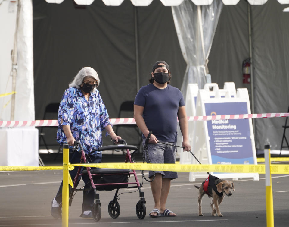 People walk after receiving their vaccines at the Disneyland Resort, serving as a Super POD (Point of Dispensing) COVID-19 mass vaccination site in Anaheim, Calif., Wednesday, Jan. 13, 2021. The parking lot is located off Katella Avenue and sits southeast of Disneyland. California is immediately allowing residents 65 and older to get scarce coronavirus vaccines, Gov. Gavin Newsom announced Wednesday. (AP Photo/Damian Dovarganes)