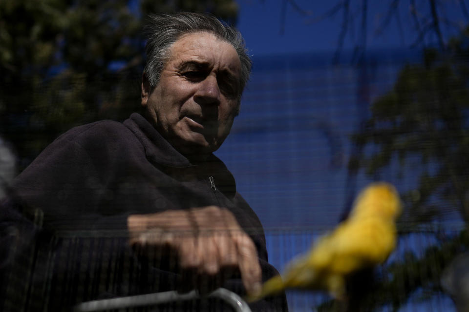 Valentin Faijoo looks at his caged birds sitting on a bench outside the San Jose Home for seniors where he lives in Tandil, Argentina, Wednesday, Sept. 15, 2021. Faijoo was allowed to take his pets to the residence during the COVID-19 pandemic lockdown and said it changed everything for good. (AP Photo/Natacha Pisarenko)
