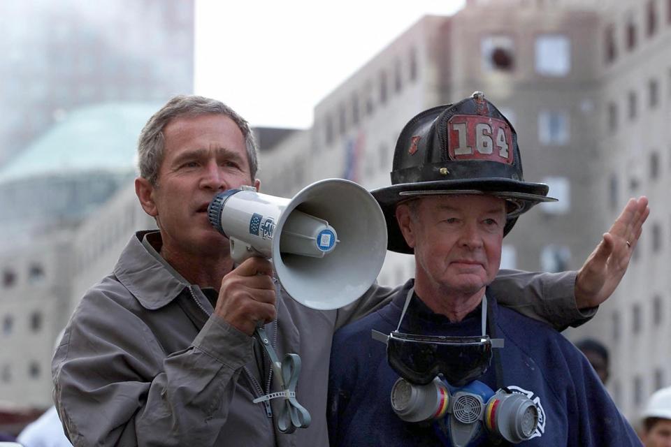 President George W. Bush, left, standing next to retired firefighter Bob Beckwith, 69, speaks to volunteers and firemen as he surveys the damage at the site of the World Trade Center in this September 2001 file photo in New York.