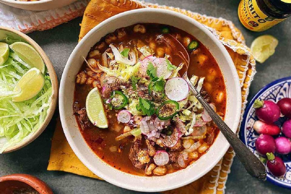 Pozole vegano rojo servido con orégano, lechuga y limón.