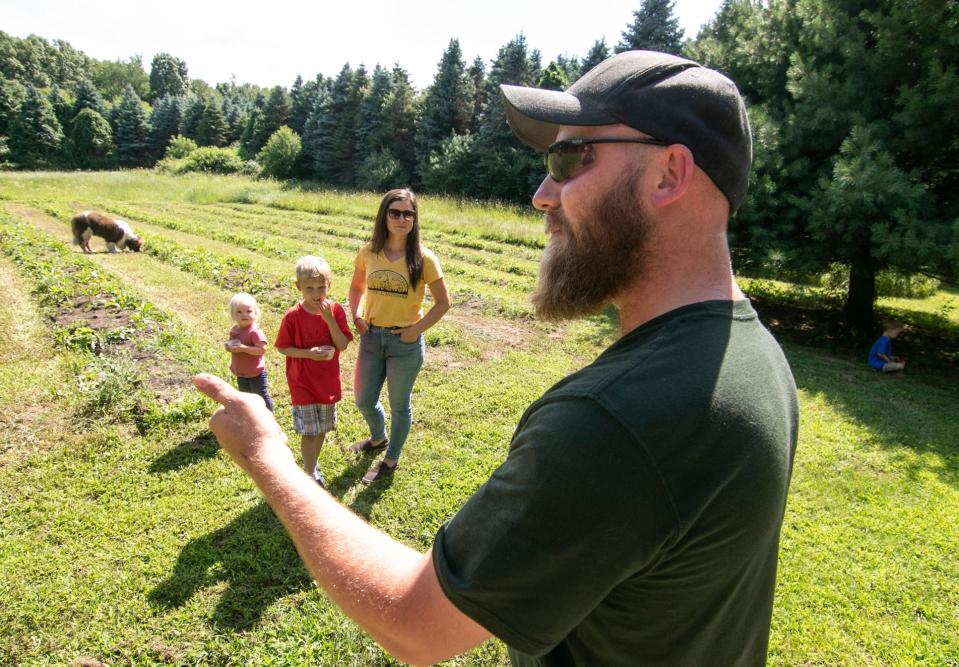 Jason Sydor talks about the planting of garlic on his family's Half Fast Homestead farm Tuesday, July 26, 2022, with (from left) his 18-month-old daughter Norah, son Ben, 6, wife Andrea and Sam, 5, (at right in the shade of a tree).