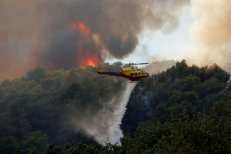 A helicopter drops water as flames and smoke from a burning wildfire fills the sky in Carros, near Nice, France, July 24, 2017. REUTERS/Eric Gaillard