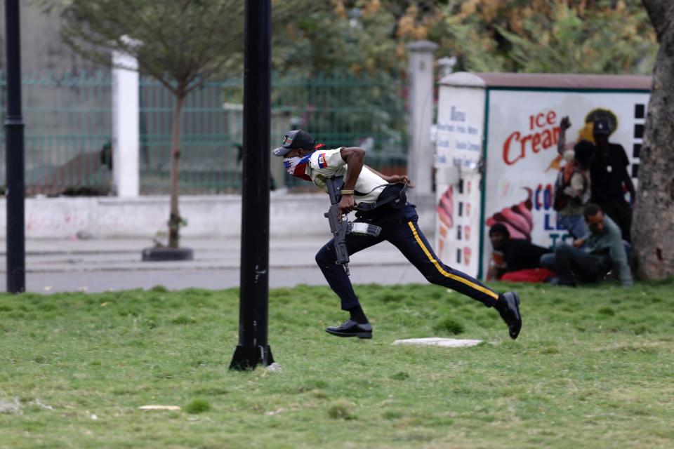 An armed police officer runs as soldiers fire in his direction during a protest over police pay and working conditions for the national police, in Port-au-Prince, Haiti, Sunday, Feb. 23, 2020.