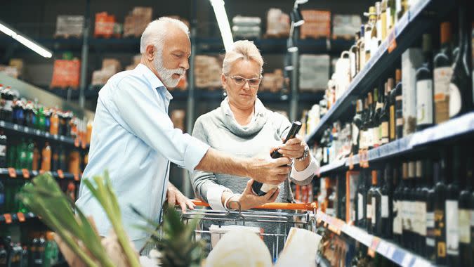 Closeup side view of early 60's couple walking through supermarket aisle and choosing some wine for tonight's dinner.