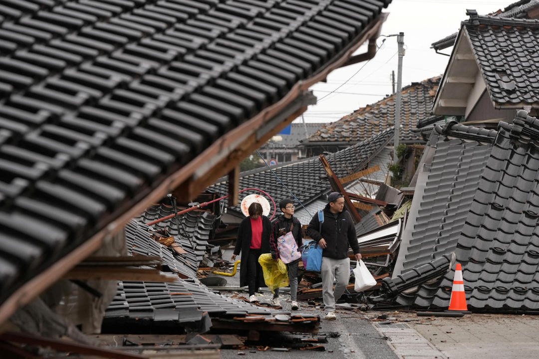 日本石川1日發生強震，珠洲市遭受海嘯破壞的住宅區，當地居民在倒塌的房屋之間行走。（Kyodo/路透社）