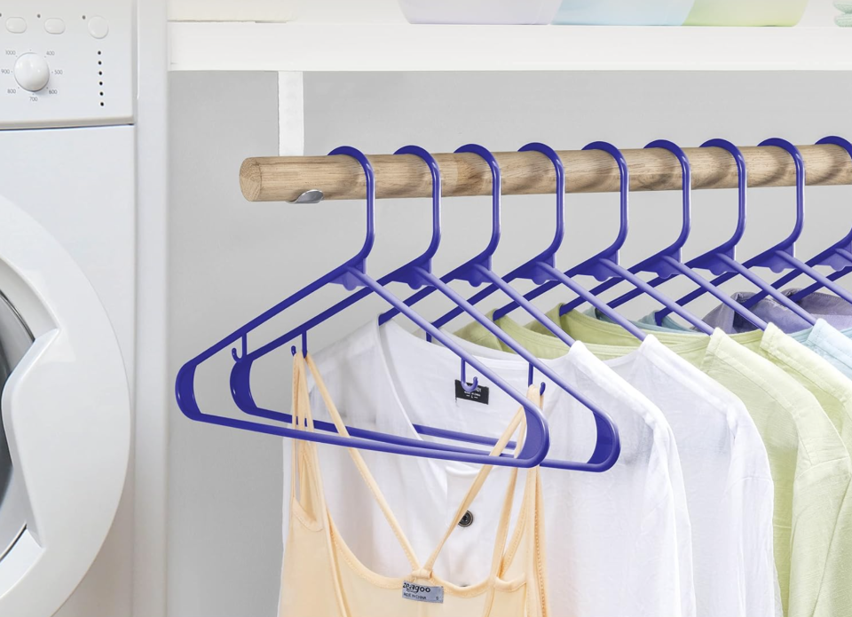 Blue hangers with wet clothes on a wooden rod in a laundry room. 