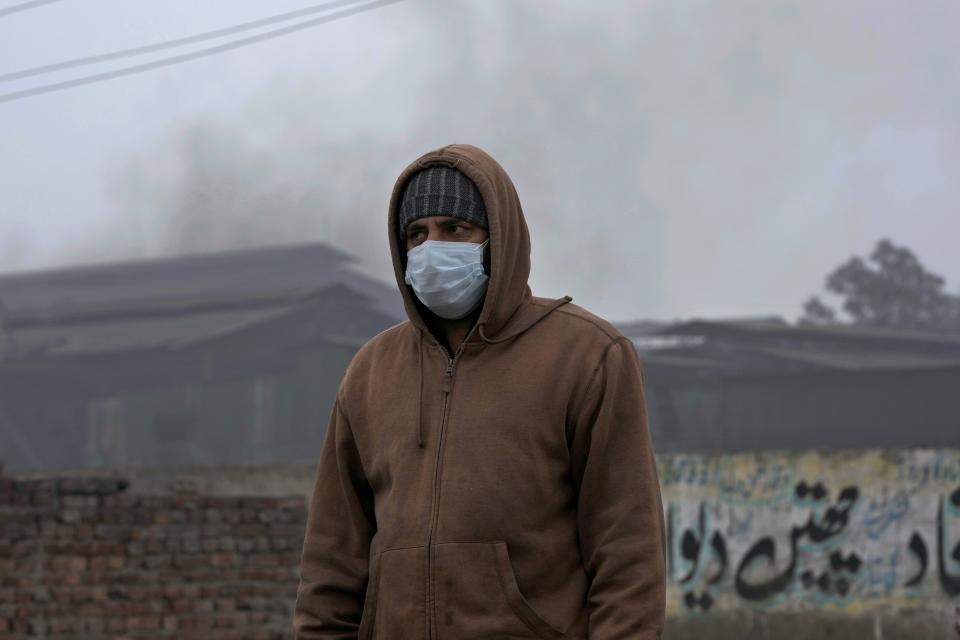 A man, wearing a mask, walks past a small iron factory releasing smoke in Lahore, Pakistan, Tuesday, Jan. 16, 2024. Toxic smog has sickened tens of thousands of people in recent months. (AP Photo/K.M. Chaudary)