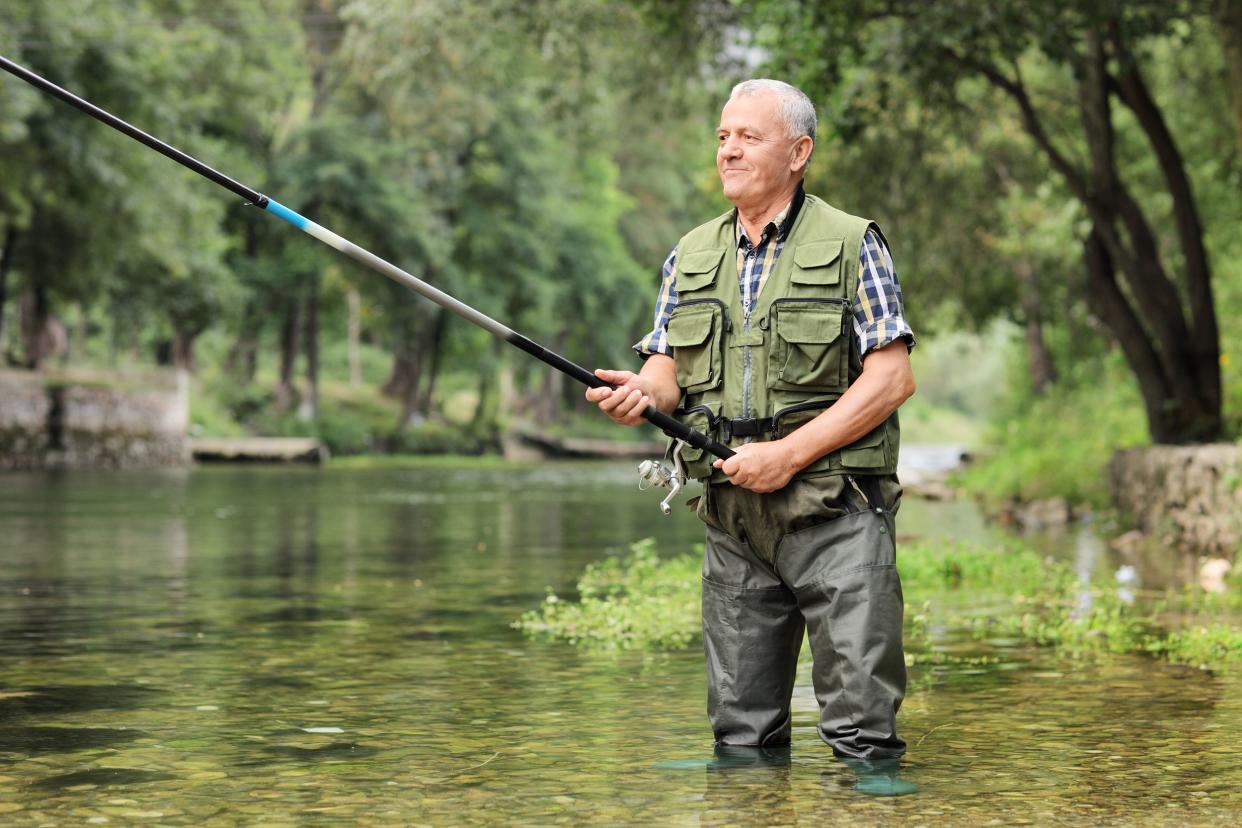 cheerful mature fisherman fishing in a river outdoors