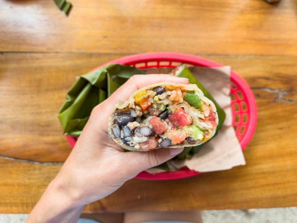 A hand holding a  burrito in a restaurant. 