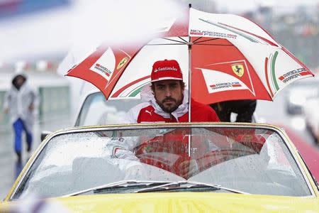 Ferrari Formula One driver Fernando Alonso of Spain sits under an umbrella during the drivers' parade ahead of the Japanese F1 Grand Prix at the Suzuka Circuit October 5, 2014. REUTERS/Yuya Shino