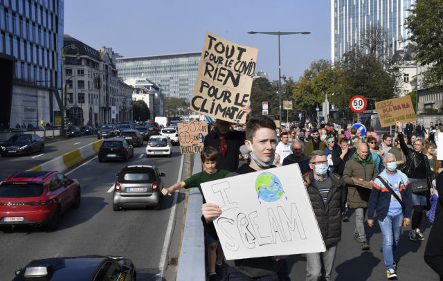 People hold signs and banners as they participate in a climate march and demonstration in Brussels, Sunday, Oct. 10, 2021. Some 80 organizations are joining in a climate march through Brussels to demand change and push politicians to effective action in Glasgow later this month. Sign at left reads in French: 'Everything for COVID, nothing for climate'. (AP Photo/Geert Vanden Wijngaert)