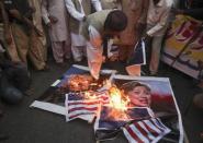 A supporter of religious political party Sunni Tehreek set ablaze the images of U.S. President Barack Obama (L), U.S. Secretary of State Hillary Clinton (R), the NATO and the U.S. flags during a demonstration in Karachi December 1, 2011. Pakistan, enraged by a NATO cross-border air attack that killed 24 soldiers, could withdraw its support for the U.S.-led war on militancy if its sovereignty is violated again, the foreign minister suggested in comments published.