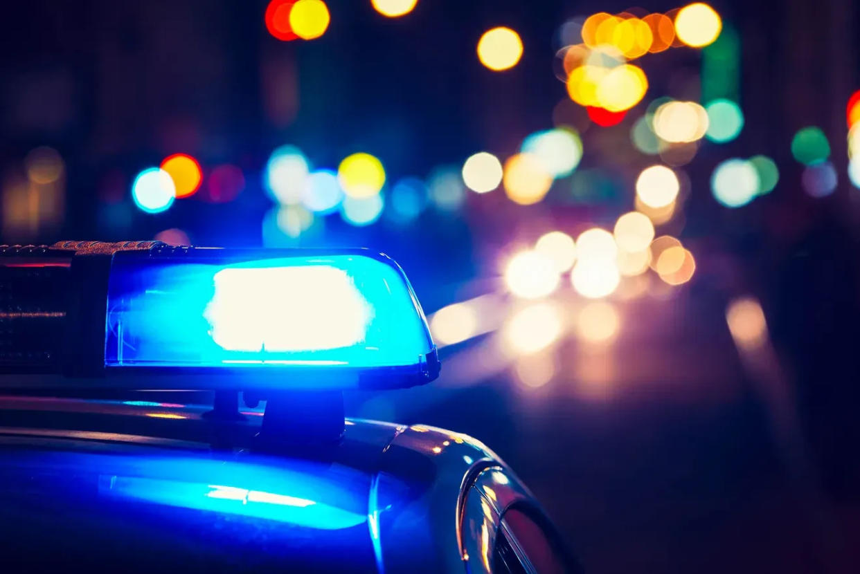 A close-up image of the flashing lights atop a squad car, as the blurry lights of other distant vehicles, businesses and traffic signals dot up the hazy nighttime background.