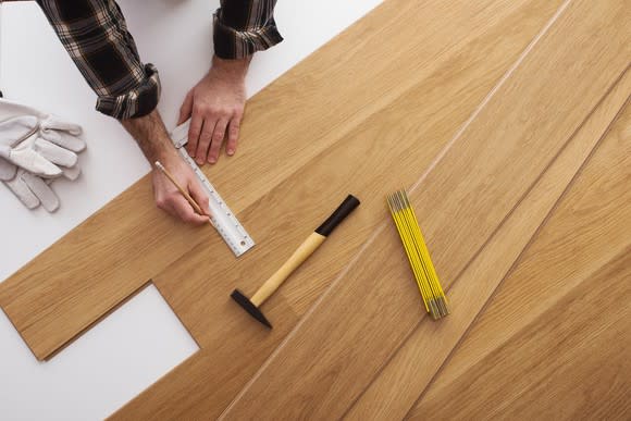 A man measuring and marking a piece of hardwood flooring to cut.