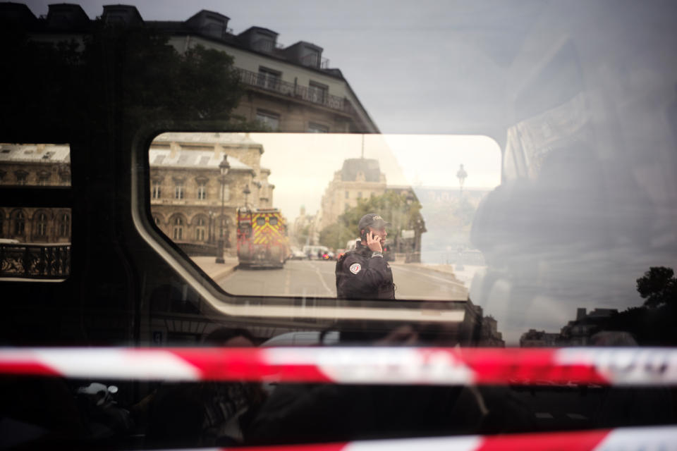 A police officer uses his phone near the Paris police headquarters, left, Thursday, Oct.3, 2019. A union official says 4 police officers have died in a knife attack by an employee at Paris police headquarters. (AP Photo/Kamil Zihnioglu)