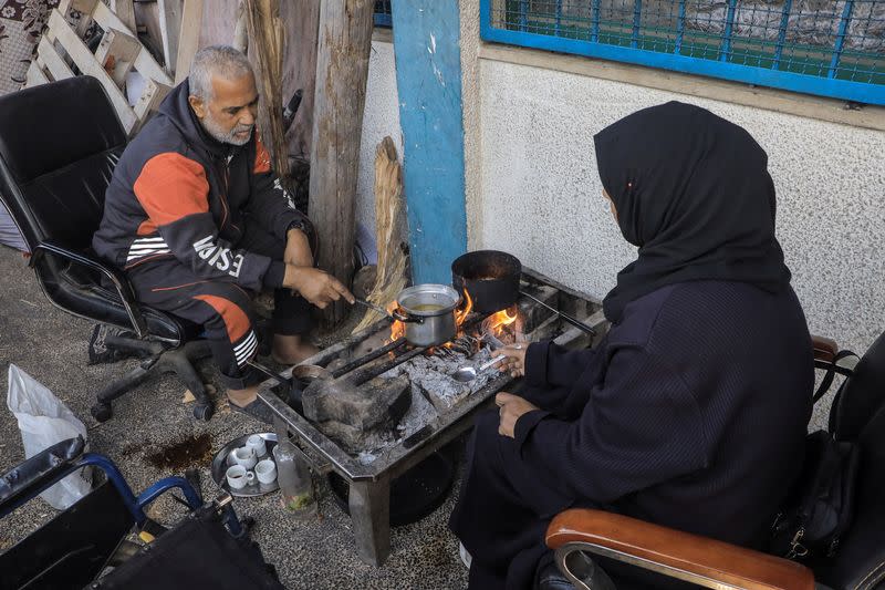A Palestinian couple cooks on a fire, in Jabalia refugee camp
