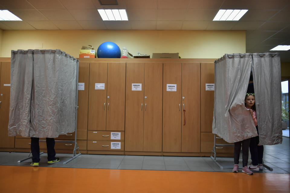 A girl peeks out of a booth as people cast their votes, at a polling station, during the general election in the small village of Tafalla, around 38 kms (23,6 miles) from Pamplona, Spain, Sunday, April 28, 2019. A divided Spain is voting in its third general election in four years, with all eyes on whether a far-right party will enter Parliament for the first time in decades and potentially help unseat the Socialist government. (AP Photo/Alvaro Barrientos)